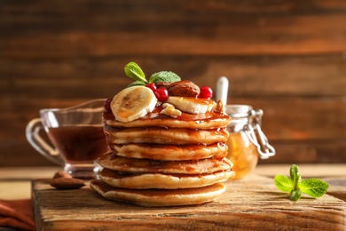 Stack of tasty pancakes with banana, berries, nuts and syrup on wooden board