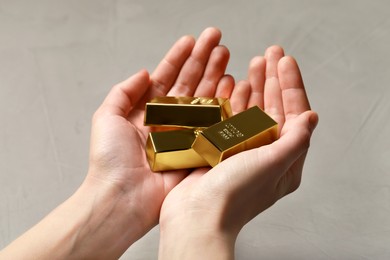 Photo of Woman holding gold bars against grey textured background, closeup