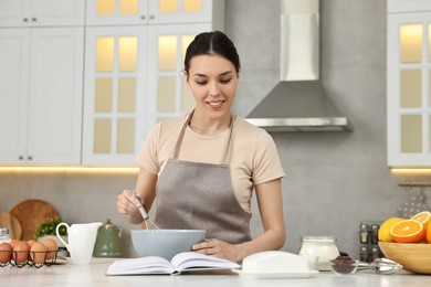 Photo of Young woman with recipe book cooking in kitchen