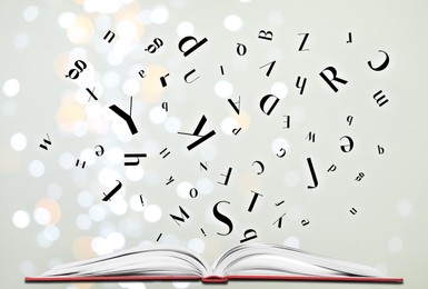 Image of Letters flying out from open book on light grey background, bokeh effect