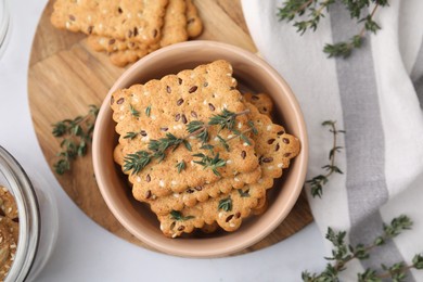 Cereal crackers with flax, sesame seeds and thyme in bowl on light table, top view