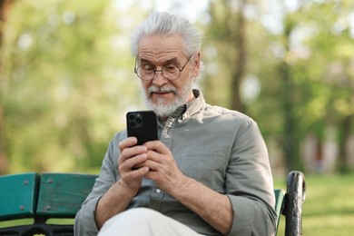 Portrait of happy grandpa with glasses using smartphone on bench in park