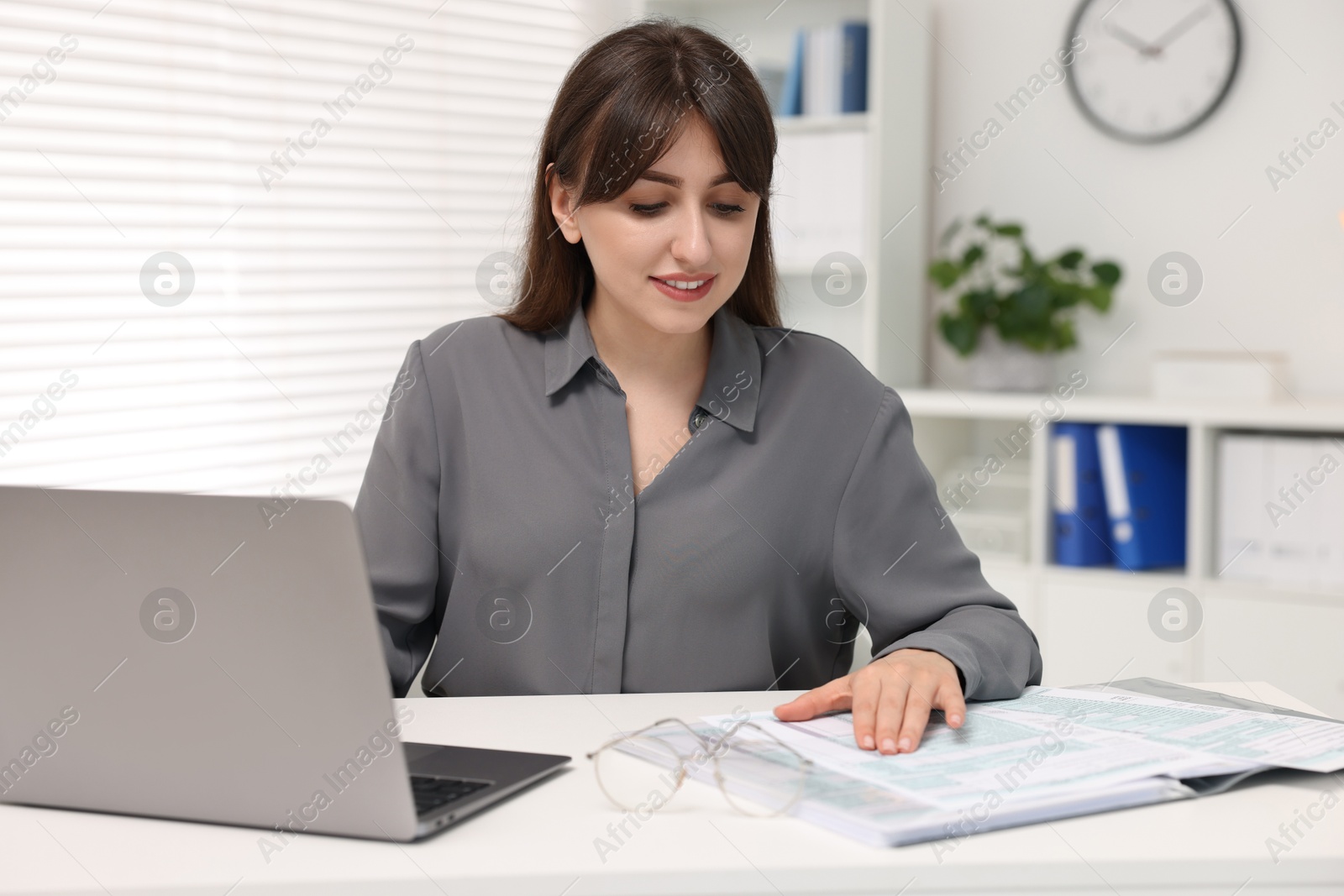 Photo of Smiling secretary doing paperwork at table in office