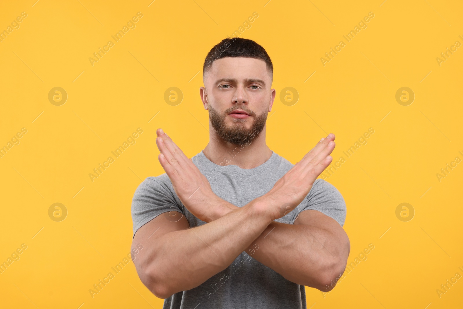 Photo of Stop gesture. Man with crossed hands on orange background