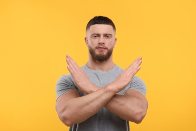 Photo of Stop gesture. Man with crossed hands on orange background