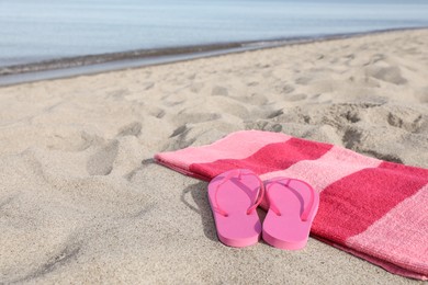 Beach towel and slippers on sand near sea, space for text