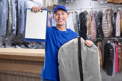 Happy courier with garment cover of clothes showing clipboard in dry-cleaning