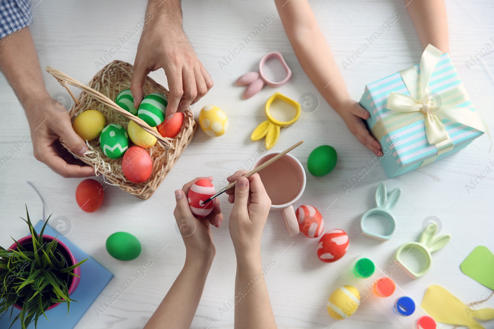 Photo of Father, mother and their child painting Easter eggs on wooden background, top view