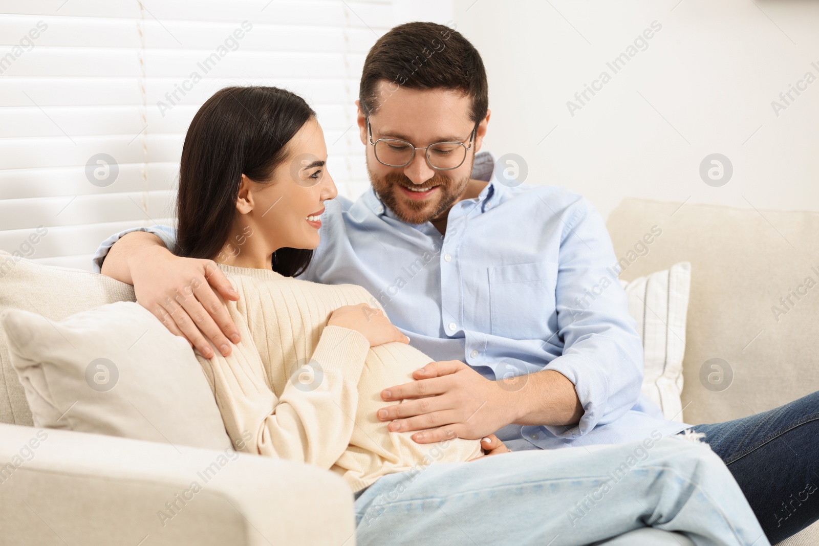 Photo of Happy pregnant woman spending time with her husband on sofa at home