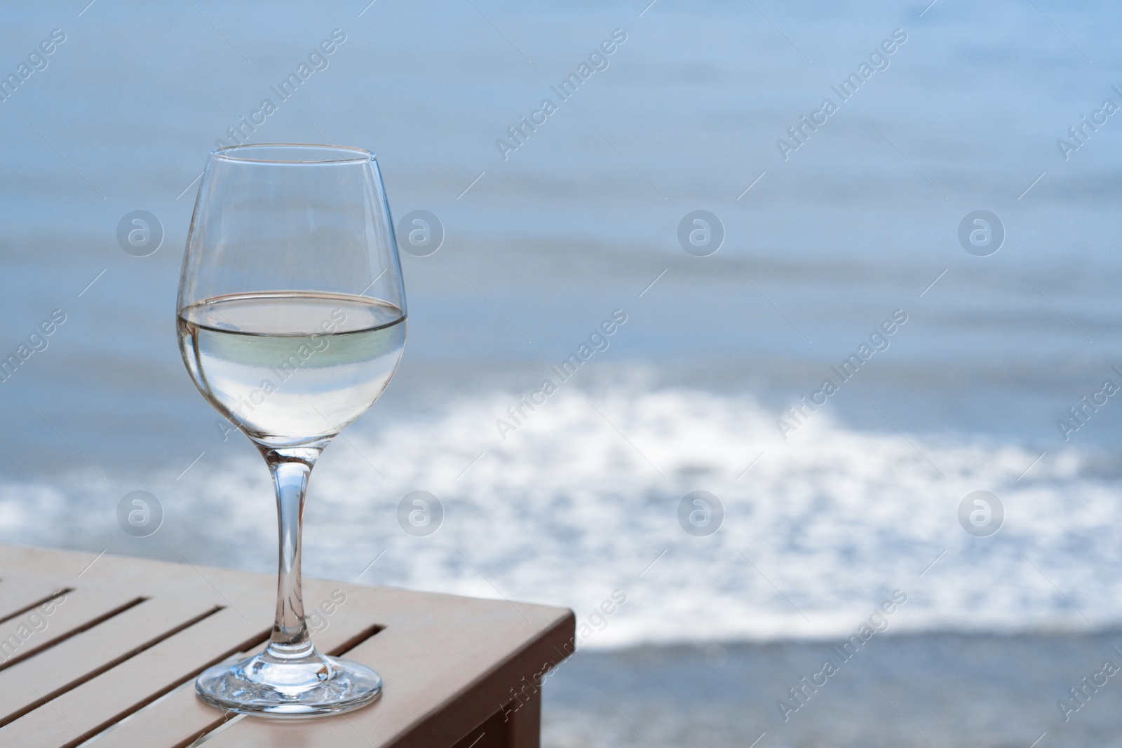 Photo of Glass with wine on table near sea. Space for text