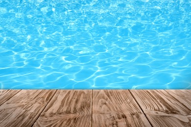 Image of Empty wooden surface near swimming pool with clear water. Space for design