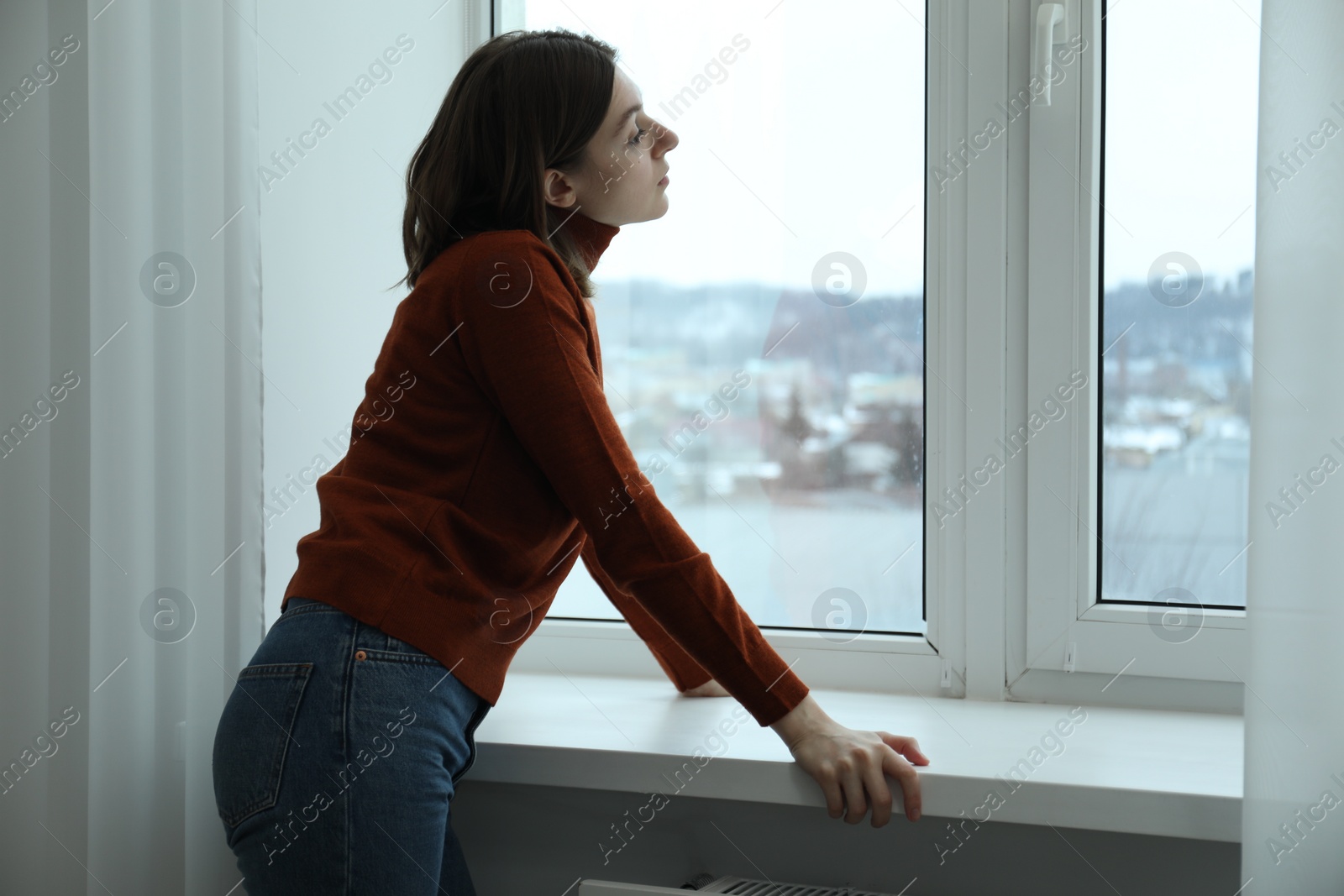 Photo of Sad young woman near window indoors, space for text