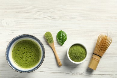 Photo of Cup of fresh matcha tea, green powder and bamboo whisk on white wooden table, flat lay. Space for text