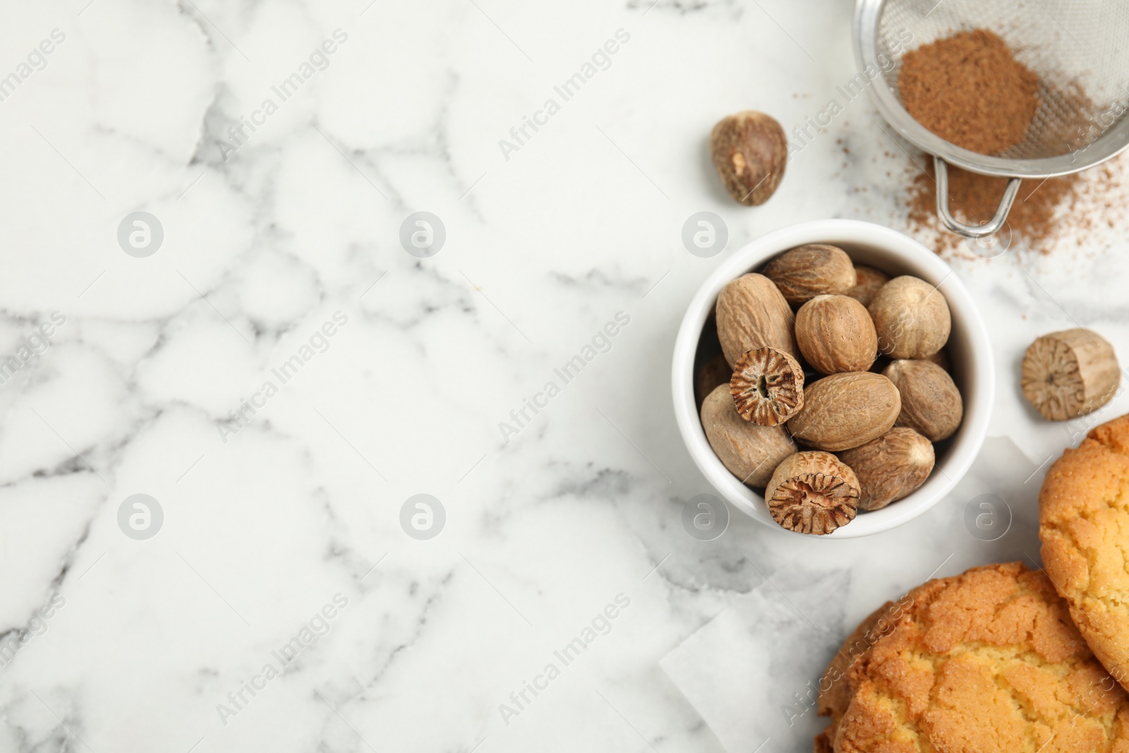 Photo of Nutmeg powder, seeds and tasty cookies on white marble table, flat lay. Space for text