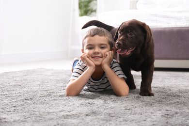 Photo of Little boy with puppy on floor in bedroom. Friendly dog