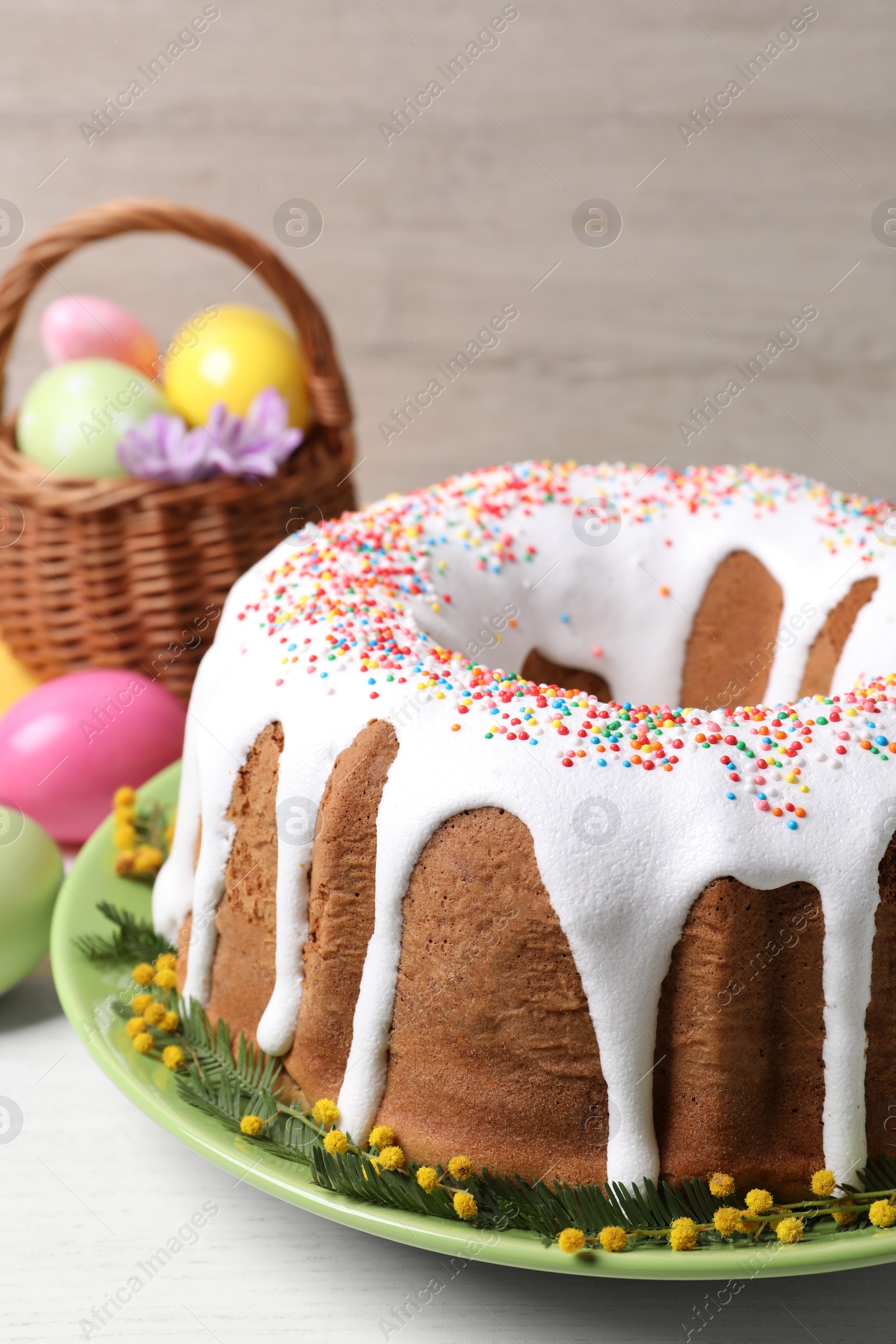 Photo of Glazed Easter cake with sprinkles and painted eggs on white wooden table, closeup