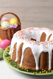 Photo of Glazed Easter cake with sprinkles and painted eggs on white wooden table, closeup