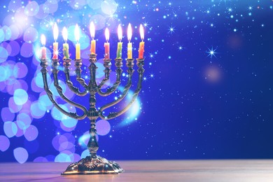 Hanukkah celebration. Menorah with burning candles on wooden table against blue background with blurred lights, space for text