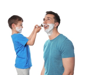 Photo of Little son applying shaving foam onto dad's face against white background