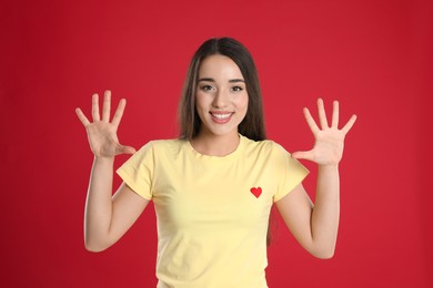 Photo of Woman in yellow t-shirt showing number ten with her hands on red background