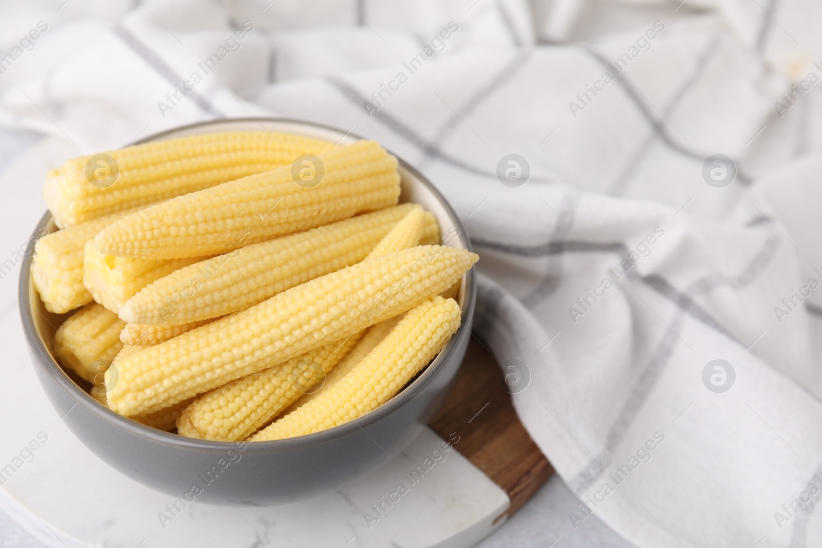 Photo of Tasty fresh yellow baby corns in bowl on white table, space for text