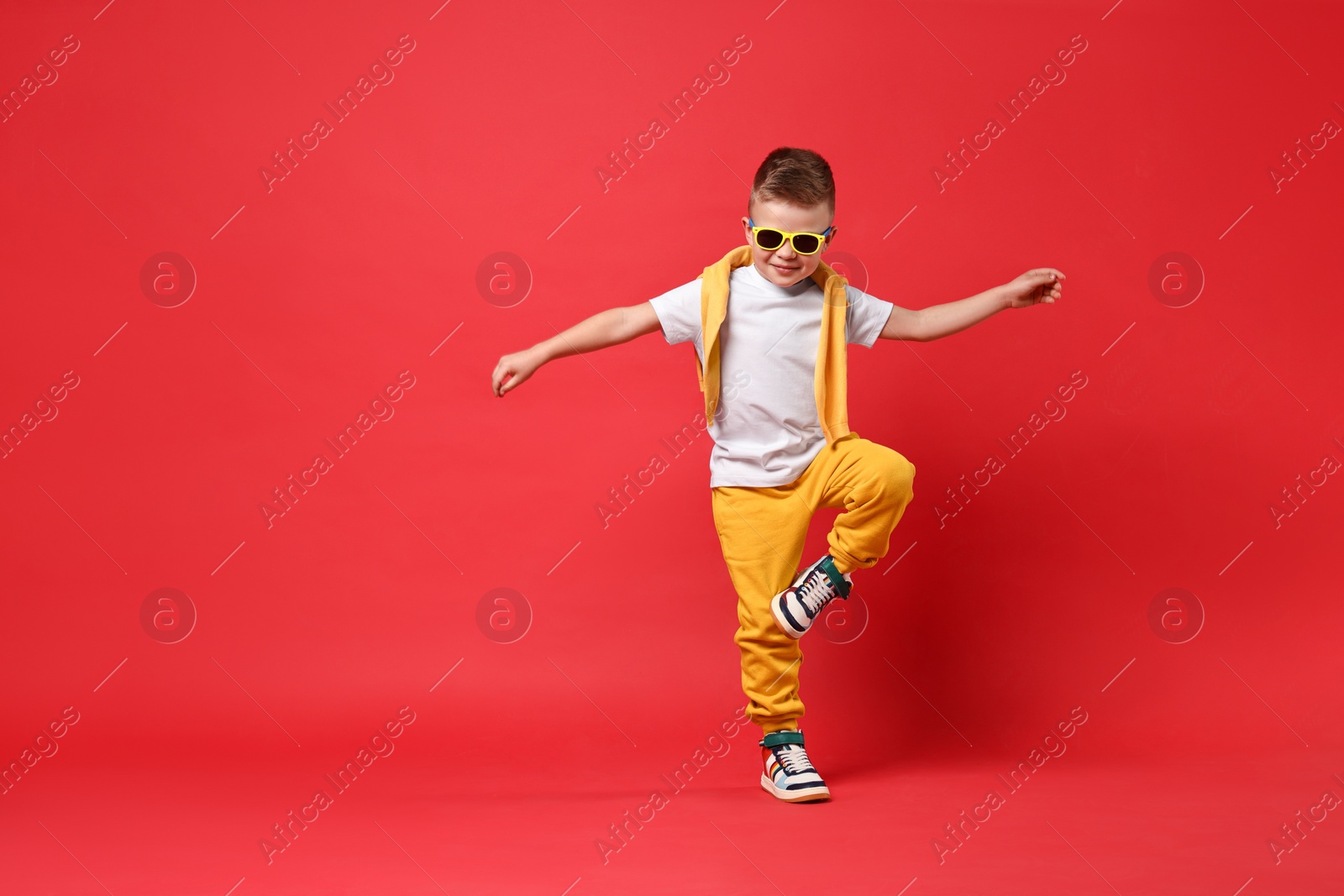 Photo of Happy little boy dancing on red background. Space for text