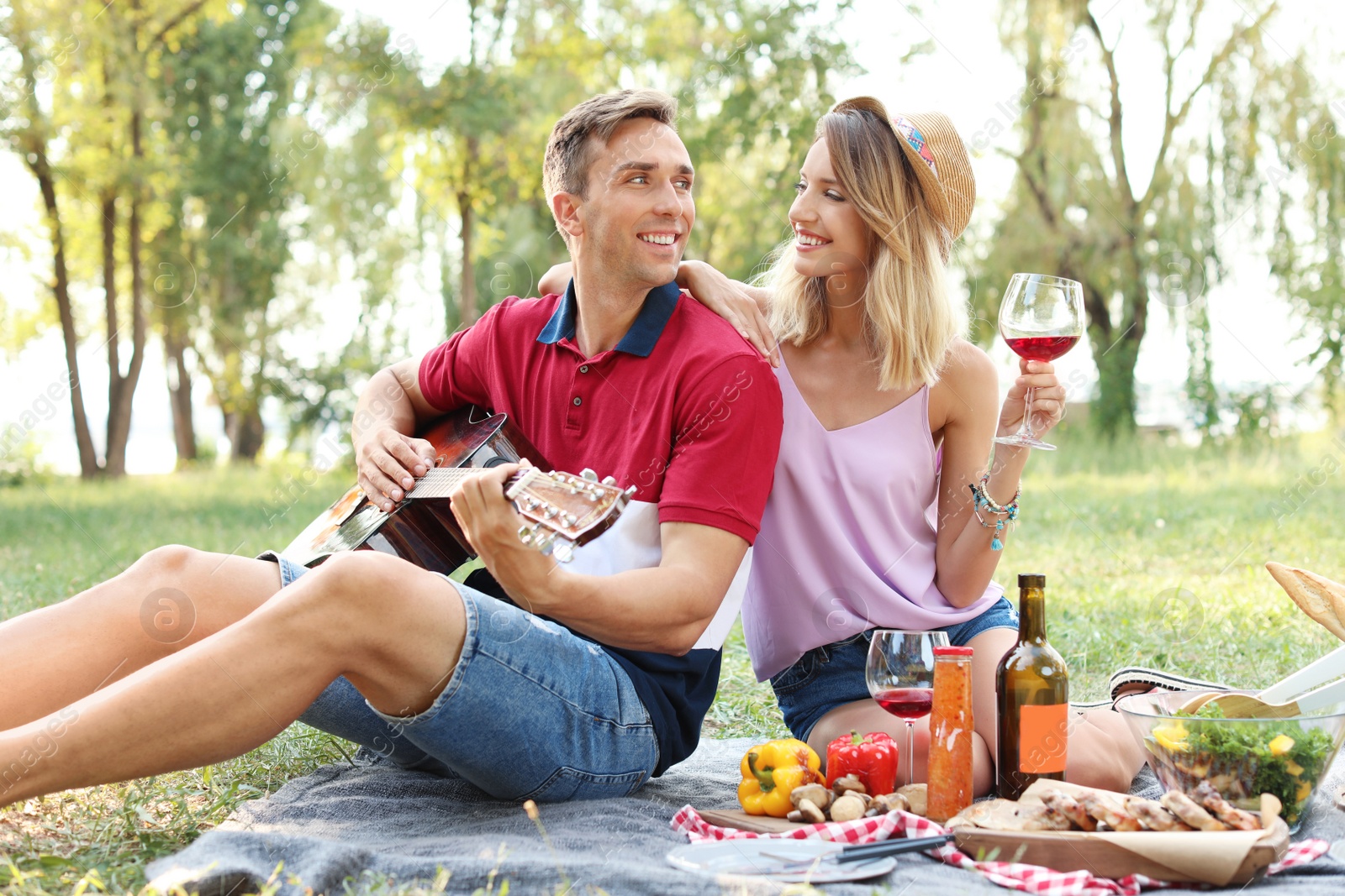 Photo of Young man playing guitar to his girlfriend in park. Summer picnic