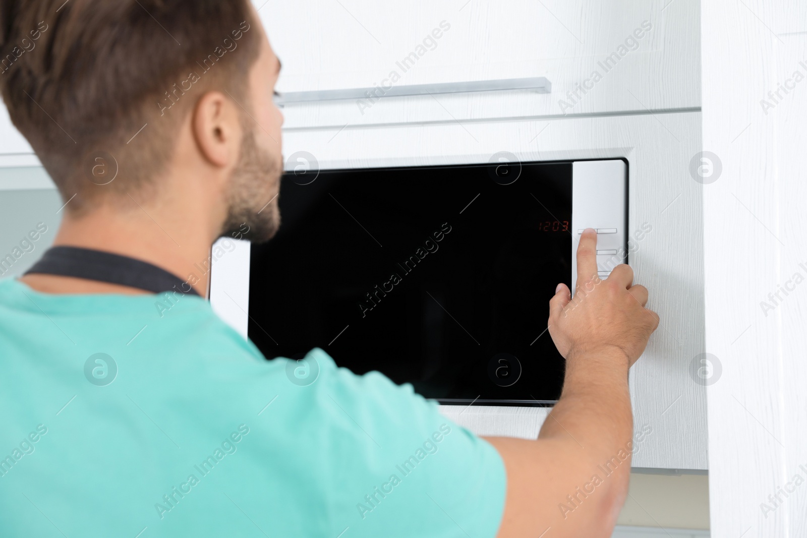 Photo of Young man using modern microwave oven at home