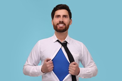 Photo of Happy businessman wearing superhero costume under suit on light blue background