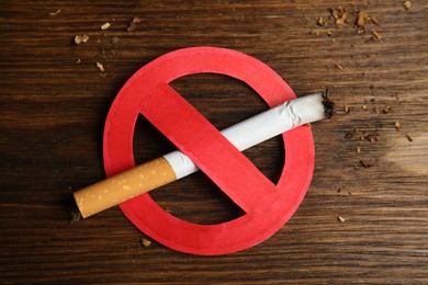 Photo of Cigarette with prohibition sign on wooden table, top view. Quitting smoking concept