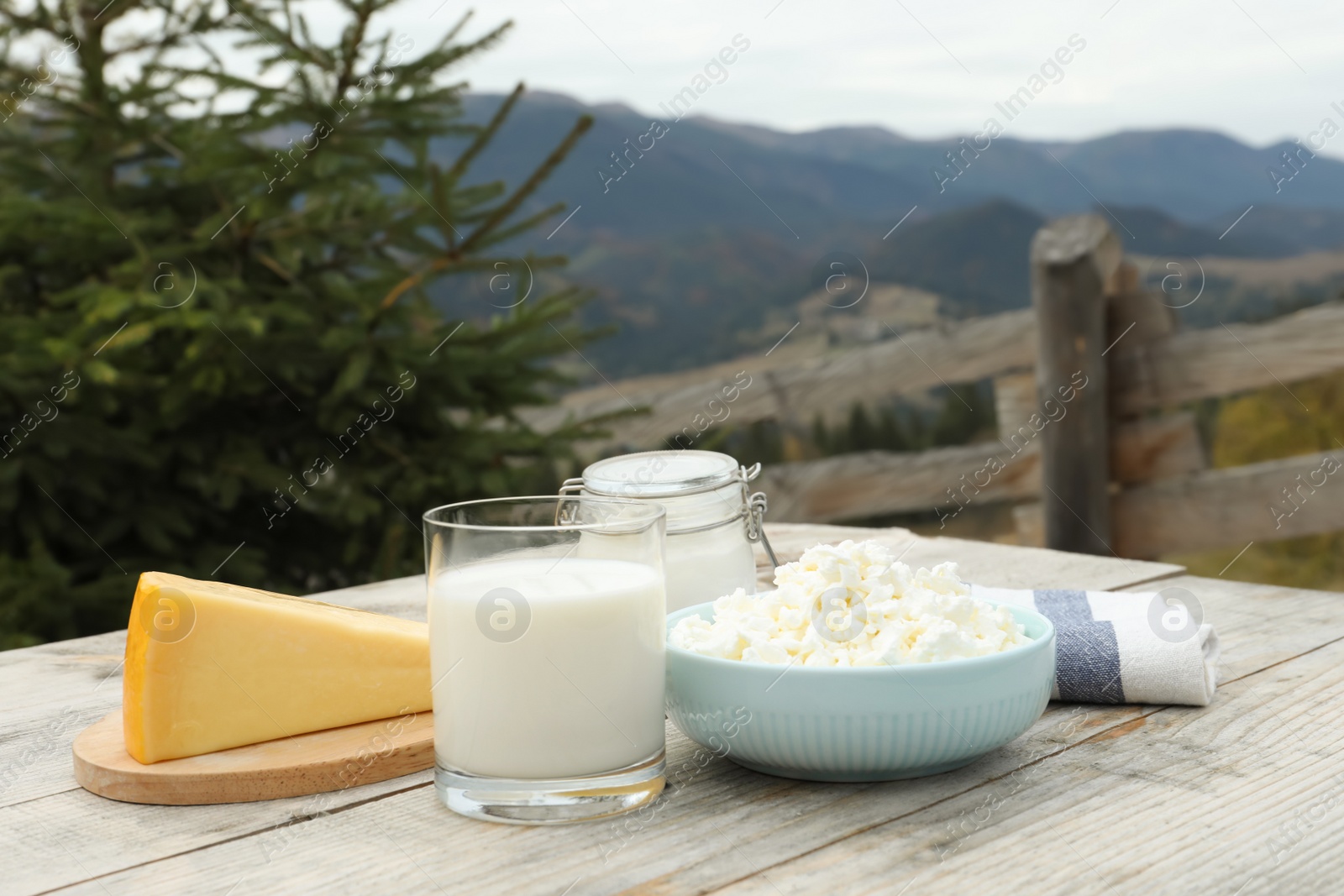 Photo of Tasty cottage cheese and other fresh dairy products on wooden table in mountains