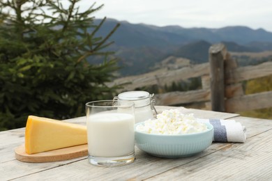 Photo of Tasty cottage cheese and other fresh dairy products on wooden table in mountains