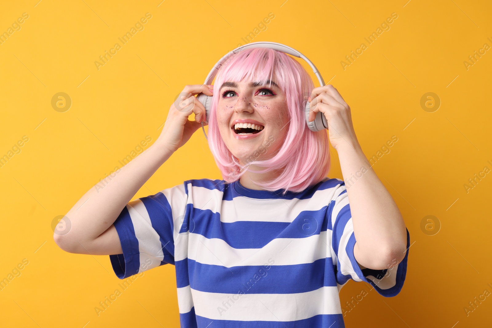 Photo of Happy woman with bright makeup and glitter freckles listening to music on yellow background