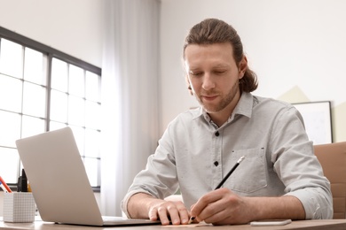 Photo of Young man working with laptop at desk in home office