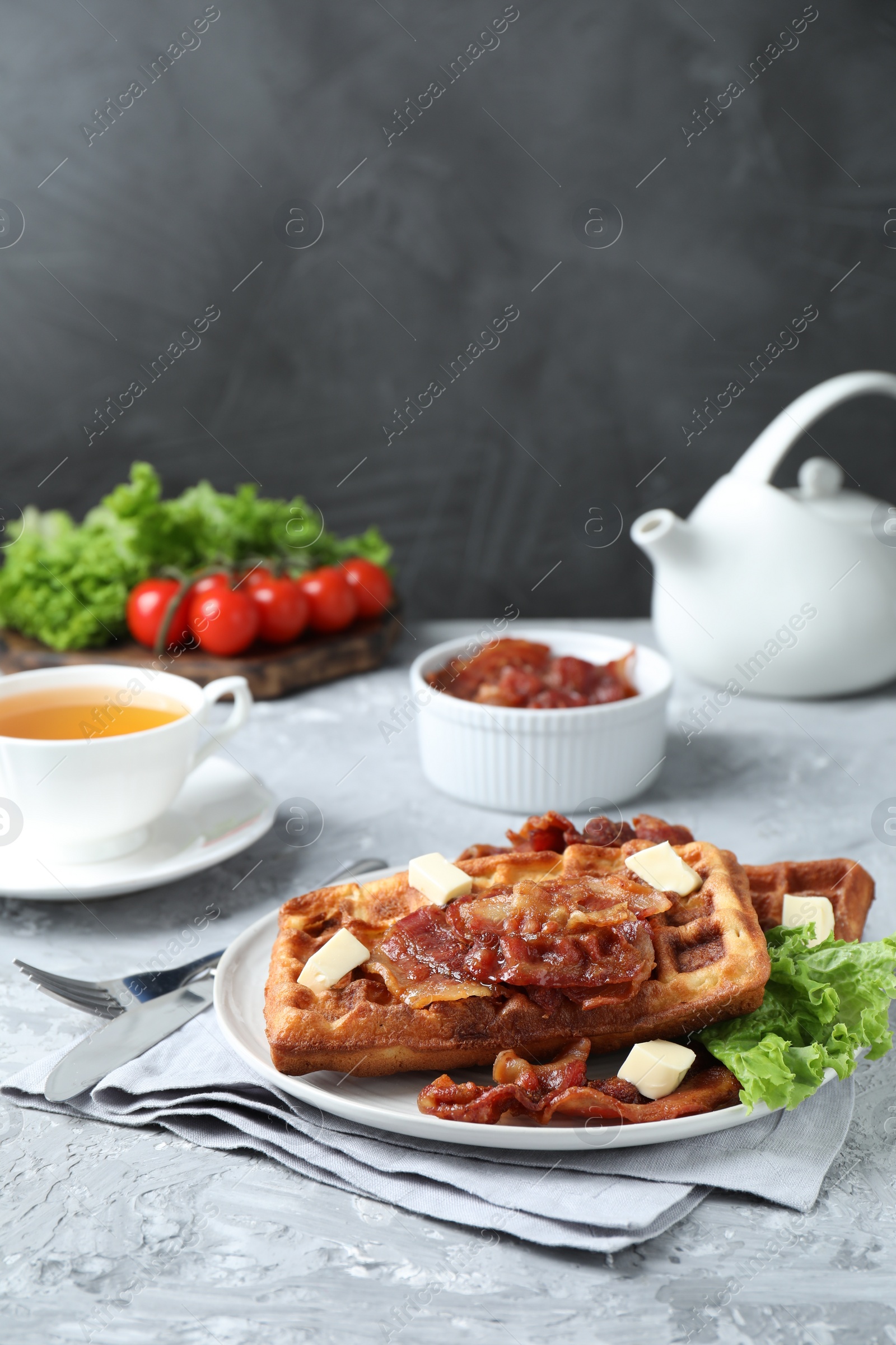 Photo of Delicious Belgium waffles served with fried bacon and butter on grey table, space for text