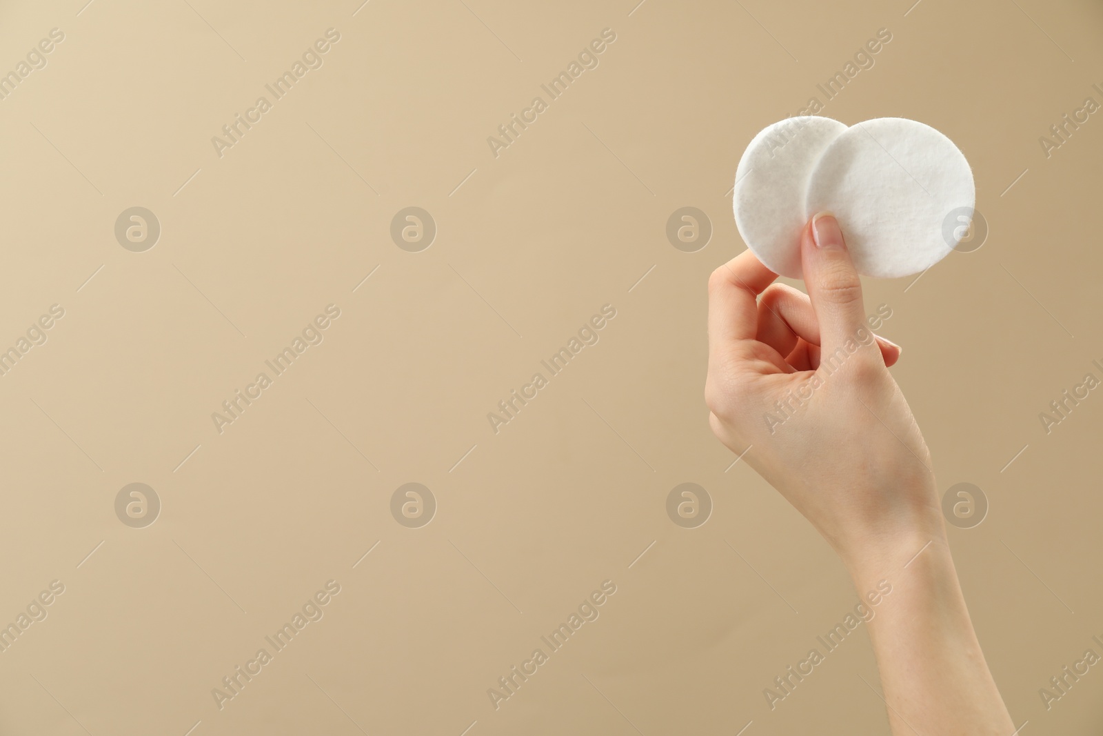 Photo of Woman holding cotton pads on beige background, closeup. Space for text