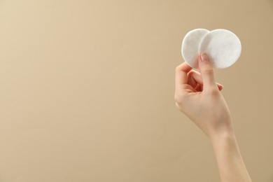 Woman holding cotton pads on beige background, closeup. Space for text