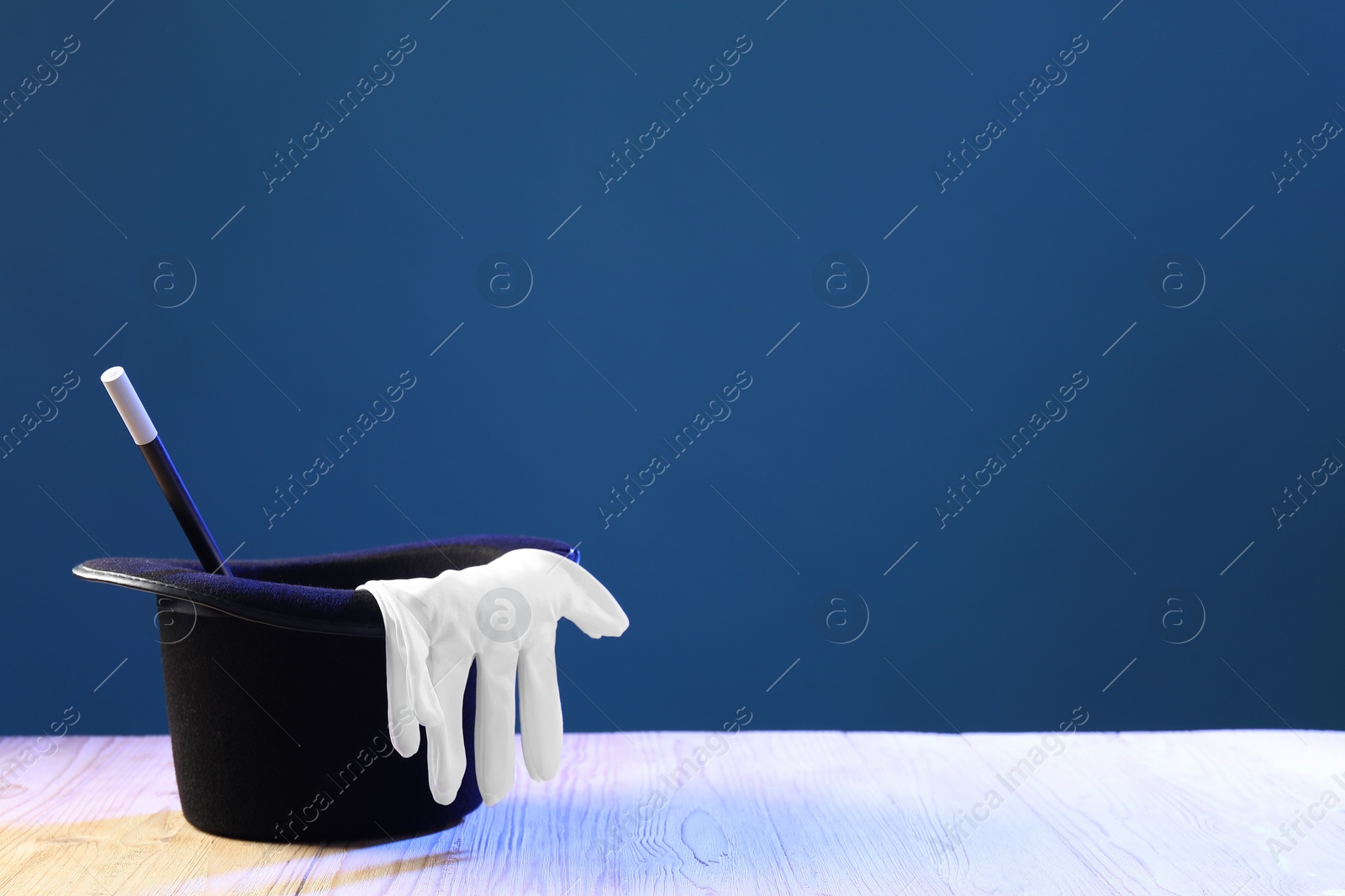 Photo of Magician's hat, wand and gloves on wooden table against blue background, space for text