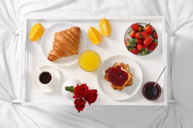 Photo of Tray with delicious breakfast on bed, top view