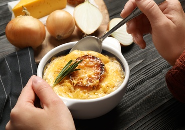 Photo of Woman eating tasty homemade french onion soup at black wooden table, closeup