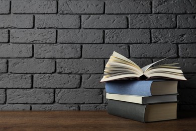 Photo of Stack of hardcover books on wooden table near dark brick wall, space for text
