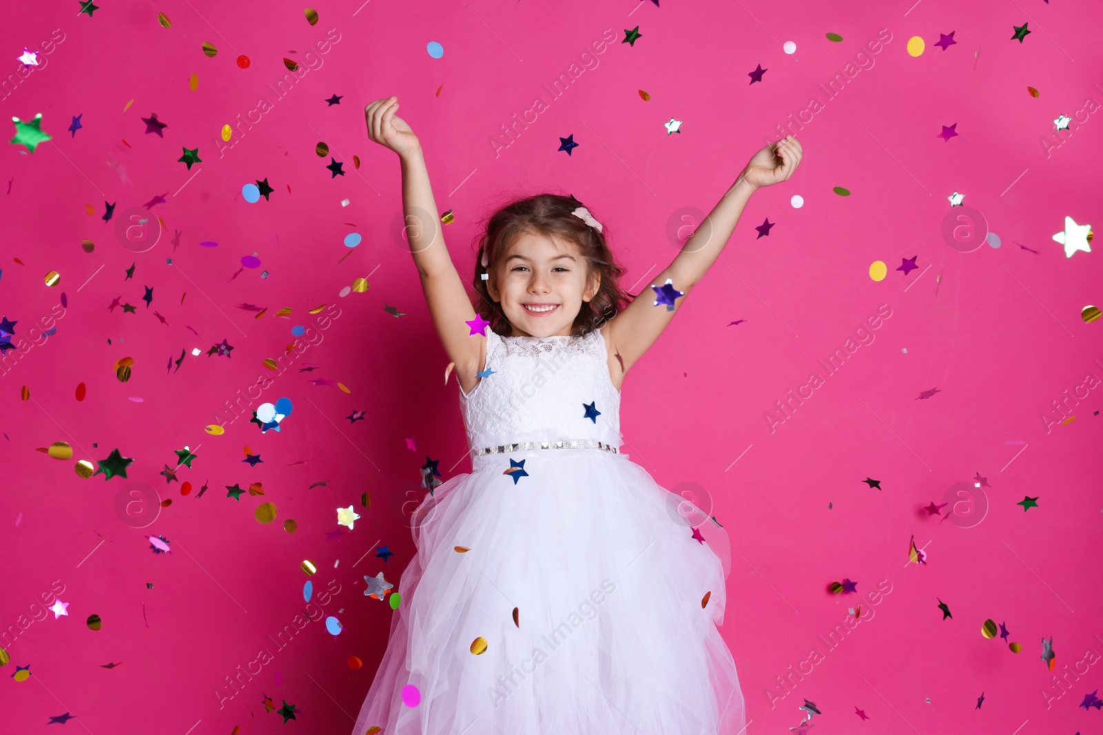 Photo of Adorable little girl and falling confetti on pink background