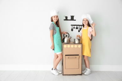 Photo of Little children in chef hats playing with carton stove indoors