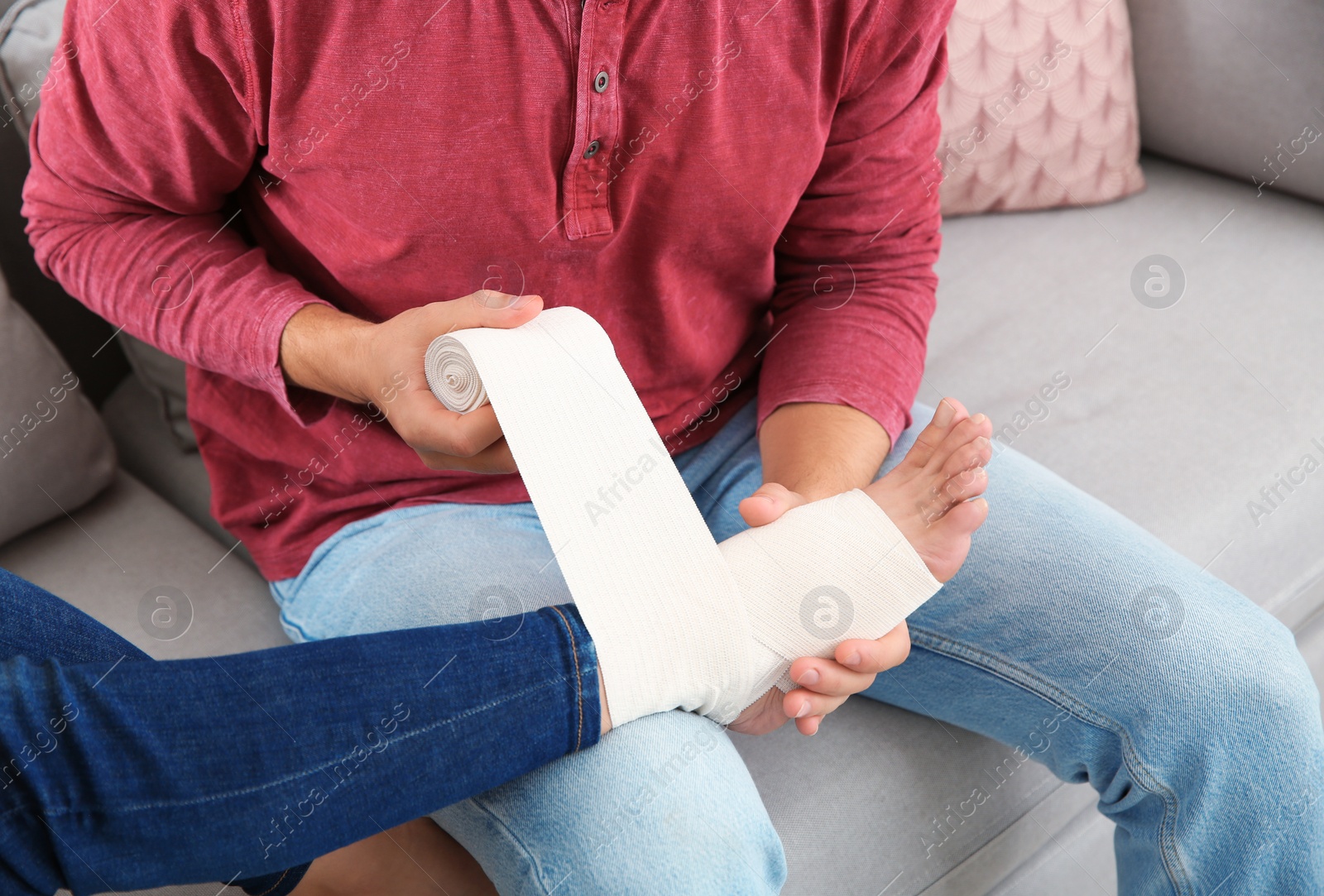 Photo of Young man applying bandage on woman's injured leg at home, closeup. First aid