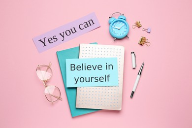 Photo of Notes with motivational quotes, glasses and office stationery on pink background, flat lay