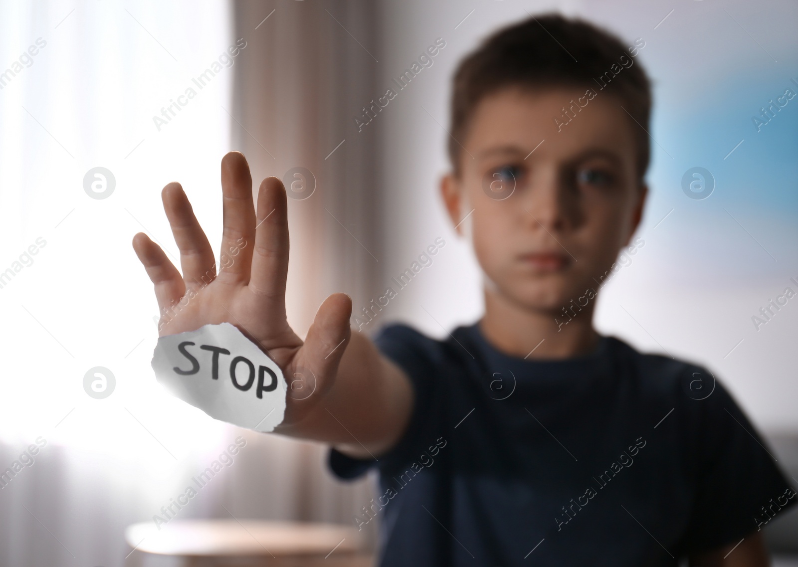 Photo of Abused little boy with sign STOP indoors, focus on hand. Domestic violence concept