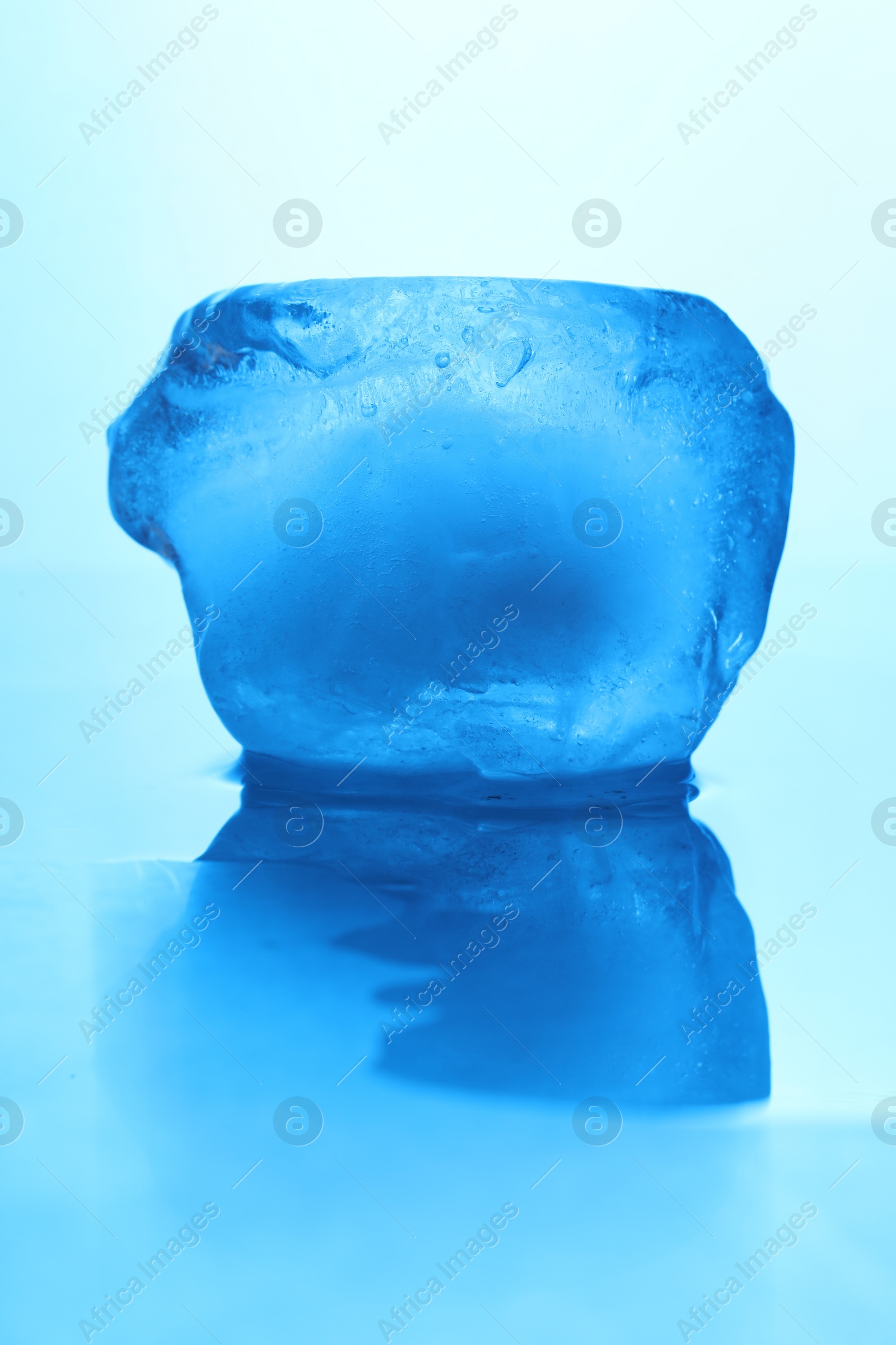 Photo of Crystal clear ice cube on light blue background, closeup. Color tone effect