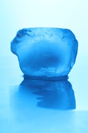 Photo of Crystal clear ice cube on light blue background, closeup. Color tone effect