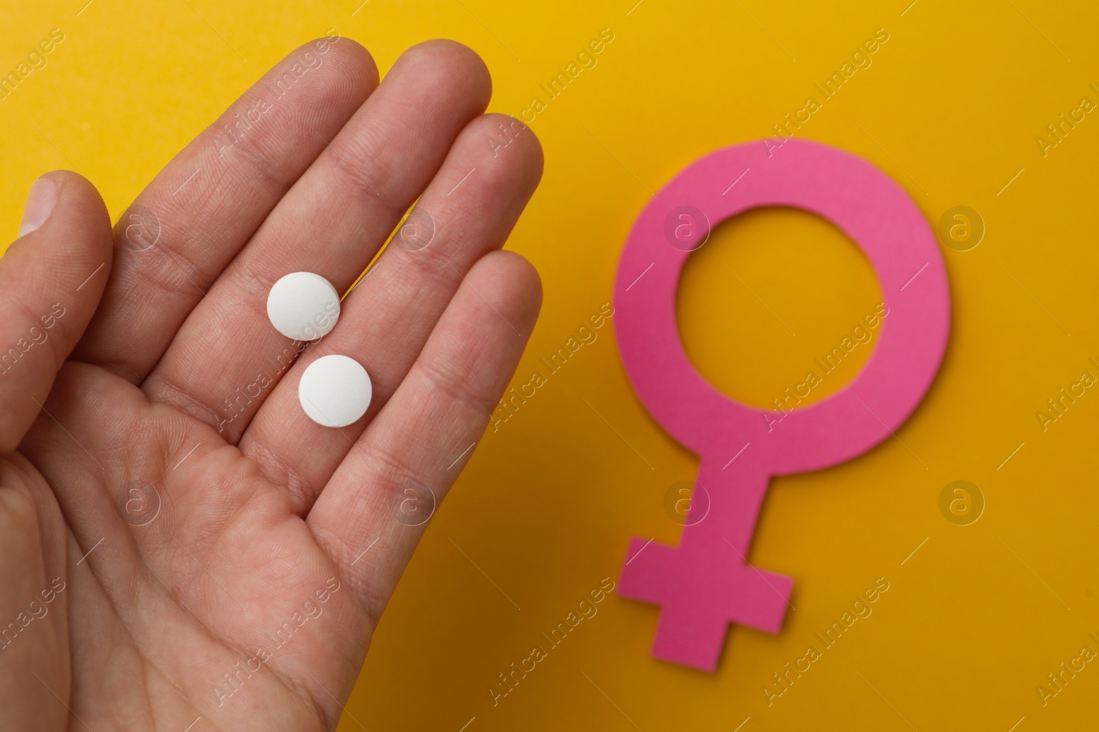 Photo of Girl holding pills near female gender sign on orange background, top view. Women's health