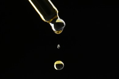 Photo of Dripping tincture from pipette on black background, closeup